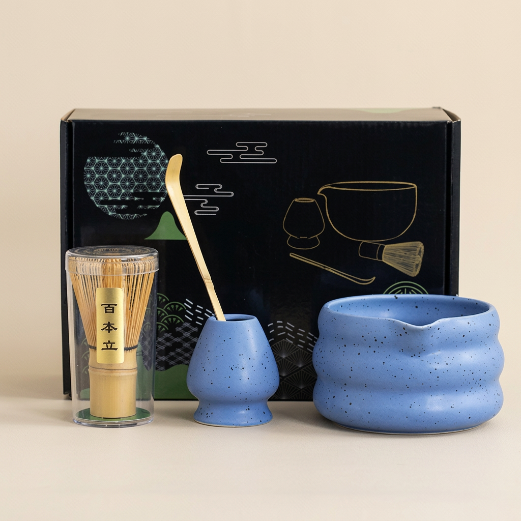 Blue matcha set on a warm beige background: speckled wavy bowl with pouring lip, whisk holder, bamboo whisk in its case and bamboo scoop, in front of its gift box