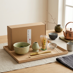 Sage matcha set on a wooden tray in a bright room, beside its kraft box and a copper kettle