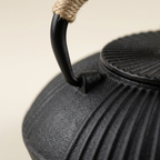 Close-up of the cord-wrapped handle and ribbed lid of the black cast iron teapot