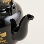 Close-up of the glossy black teapot spout and its gold painted detail