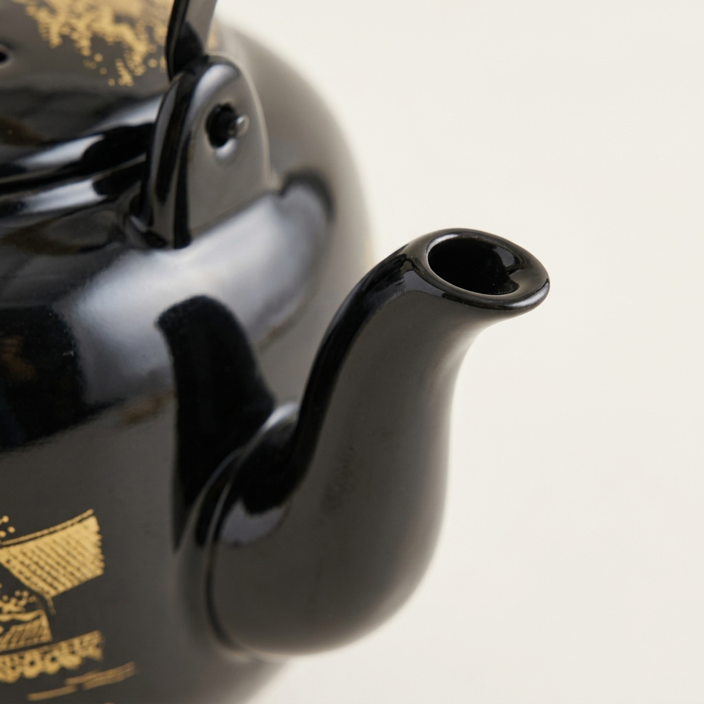 Close-up of the glossy black teapot spout and its gold painted detail