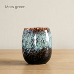 Moss green glazed tea cup without a handle on a light oak table