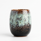 Egg-shaped glazed tea cup in moss green, with a flowing speckled glaze over a dark brown base, front view