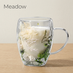 Meadow design: glass cup with dried white and green flowers, filled with milk, on a light oak table