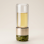 Glass tea infuser bottle in gold on a warm cream background