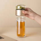 Hand unscrewing the tea chamber of the glass infuser bottle, filled with loose leaves