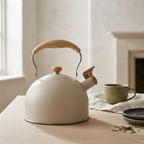 Beige Vintage Whistling Kettle on a wooden kitchen table beside a green mug