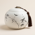 Round white ceramic tea caddy with the Bamboo design and a brown tassel, on a warm beige background